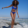 Cobalt blue bikini with broderie detail on girl balancing on rocks by the sea