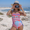 woman in pink palm print, ruched side swimsuit with camera and straw hat