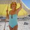 blonde woman in aquamarine trim bandeau swimsuit under yellow umbrella on the beach